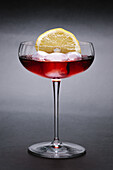 Wineglass with tasty alcoholic cocktail served with ice cubes and slice of sour lemon on gray background in light studio