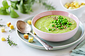 Delicious healthy cream pea soup in a bowl garnished with green peas and croutons on table