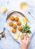 Top view of cropped unrecognizable cook hand with Arancini rice balls placed on metal tray on table with lemon and cutlery