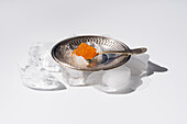 From above orange tobiko caviar served on silver plate with ice with spoon on white background