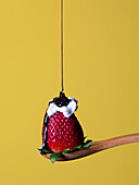 Sweet chocolate syrup pouring on ripe red strawberry with white whipped cream on wooden spoon against yellow background in light studio