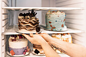 Unrecognizable woman putting fresh tasty cake with creative decorations in refrigerator while working in bakery