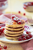 A stack of pancakes with red currants and agave syrup