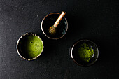 Matcha-Tee mit Matchabesen und Teepulver in Schälchen auf dunklem Untergrund