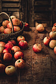 Äpfel in Weidenkorb und auf rustikalem Holztisch