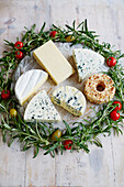 A cheese platter decorated with a rosemary and cherry tomato wreath