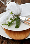 White place setting with cloth napkin and pea pod as place card