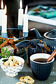 Christmas tea with cinnamon sticks and sprinkled biscuits, in front of metal candlesticks