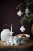 Eucalyptus branches with paper stars, teapot, biscuits, cup and snowman candle holder
