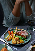 Beef Wellington wrapped in spinach and bacon and served with roasted root vegetables and peas