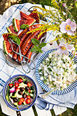 Grilled watermelon, sausages, potato salad with herbs and salad with cucumber and olives