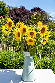 Gelbe Sonnenblumen in einer Blechvase auf einem Gartentisch