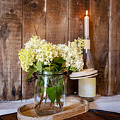 Weisse Hortensien in einer Vase, Flasche mit Kerze im Hintergrund, Etikett Strandwein