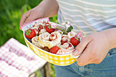 Hand holding bowl of puff pastry hearts filled with strawberry jam in the garden