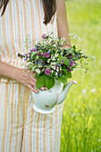 Frau hält Porzellankanne mit Wiesenblumenstrauß