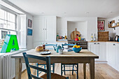 White painted kitchen with colourful accessories, table with chairs in the middle