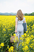 Frau mit Korb geht durch blühendes Rapsfeld (Brassica napus)