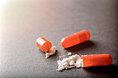 Open orange capsule with white powder drug, conceptual image