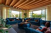 A blue upholstered suite in front of open terrace doors in a room with a woodbeamed ceiling