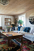 Gemütliches Sofa mit Kissen, Couchtisch aus Holz und Kelimteppich in ländlichem Wohnzimmer