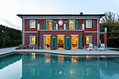 Blick über Pool auf zweigeschossige Villa mit grünen Fensterläden