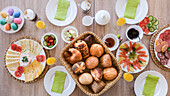 An Easter breakfast table laid with coloured eggs, rolls, salmon, and cheese and meat platter