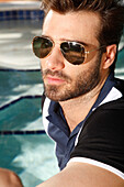 Young man with a beard and sunglasses in a polo shirt at the pool