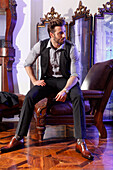 Elegant young man with beard sits on leather armchair