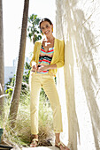 Young brunette woman wearing a striped tankini top, yellow pants and jacket