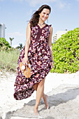 Brunette woman in printed sundress barefoot in the sand