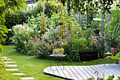 Gerundete Holzterrasse und üppige Bepflanzung mit Blumen in sommerlichem Garten