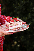 A woman holding a plate of strawberry tiramisu