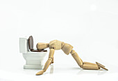 Wooden doll vomiting in a toilet, conceptual image