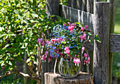 Blumenstrauß Tränendes Herz (Dicentra Spectabilis) und Kaukasus-Vergissmeinnicht (Myosotis) auf Baumstumpf