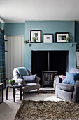 Bequeme Sessel vor Kaminofen im Zimmer mit blauen Wänden