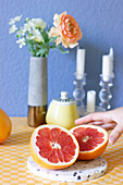 Halved grapefruit, vase with flowers and candles on table with yellow gingham tablecloth