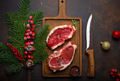 Two raw uncooked meat beef steaks on wooden cutting board with Christmas decoration