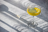 Limocello drink with lemon slice in sun light with shadows