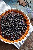 Tart with chocolate mass and blueberries, sprinkled with dried cornflower flakes and powdered sugar