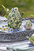 Kräuterbutter in Eiform mit Schnittlauch, Petersilie, Knoblauch, Thymian, dekoriert mit Gänseblümchen auf Silbertablett