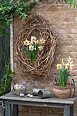 Clematis wreath hanging on a stone wall and daffodils (Narcissus) in a pot, eggs in a basket, Easter decoration