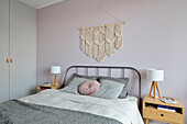 Schlichtes Doppelbett, darüber Makramee und Einbauschrank im Schlafzimmer