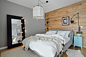 Doppelbett vor Bretterwand im Schlafzimmer, großer Spiegel mit Lichterkette vor grauer Wand