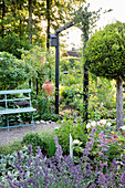 Sitzplatz neben Portal im Garten, im Vordergrund blühende Katzenminze (Nepeta)