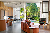 Seating area with organically shaped sofa in front of kitchen counter and bar stools in open-plan living room