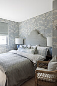 Double bed with high headboard and matching bedspread, wallpaper with tree motif on the walls