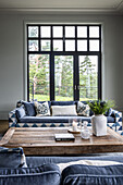 Blue and white upholstered sofas and wooden coffee table in room with French windows