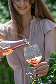 Garden party in summer: Young woman pours rosé sparkling wine into glass