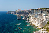 Blick über eine felsige Bucht entlang zerklüfteter Kalksteinklippen auf die ferne Zitadelle, Bonifacio, Corse-du-Sud, Korsika, Frankreich, Mittelmeer, Europa