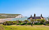 Walkers pass the Coastguard Cottages at Cuckmere Haven, with the beach and the Seven Sisters cliffs behind, East Sussex, England, United Kingdom, Europe
